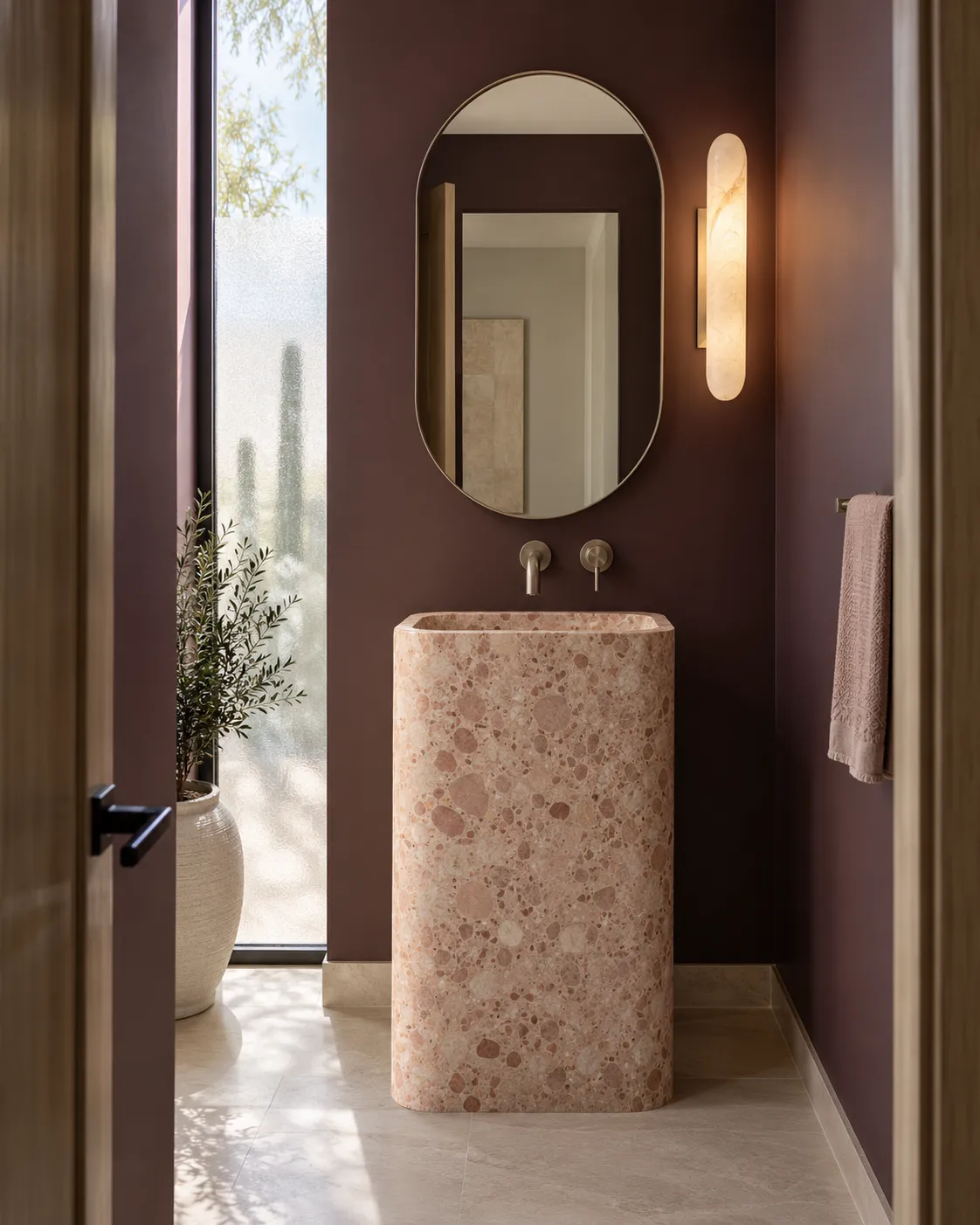 Small plum powder room with a rose terrazzo pedestal basin, an oval mirror and a tall wall light
